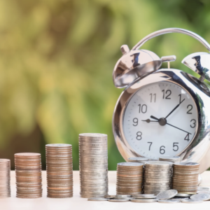 Stacked coins and a clock on a wooden desk